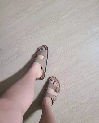 Beige sandals worn on a light wooden floor