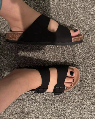 Black sandals with cork sole worn on a textured surface